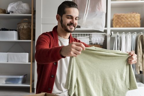 Un homme tient un t-shirt ouvert dans ses mains et le regarde comme pour se demander s'il le conserve ou s'il s'en sépare.